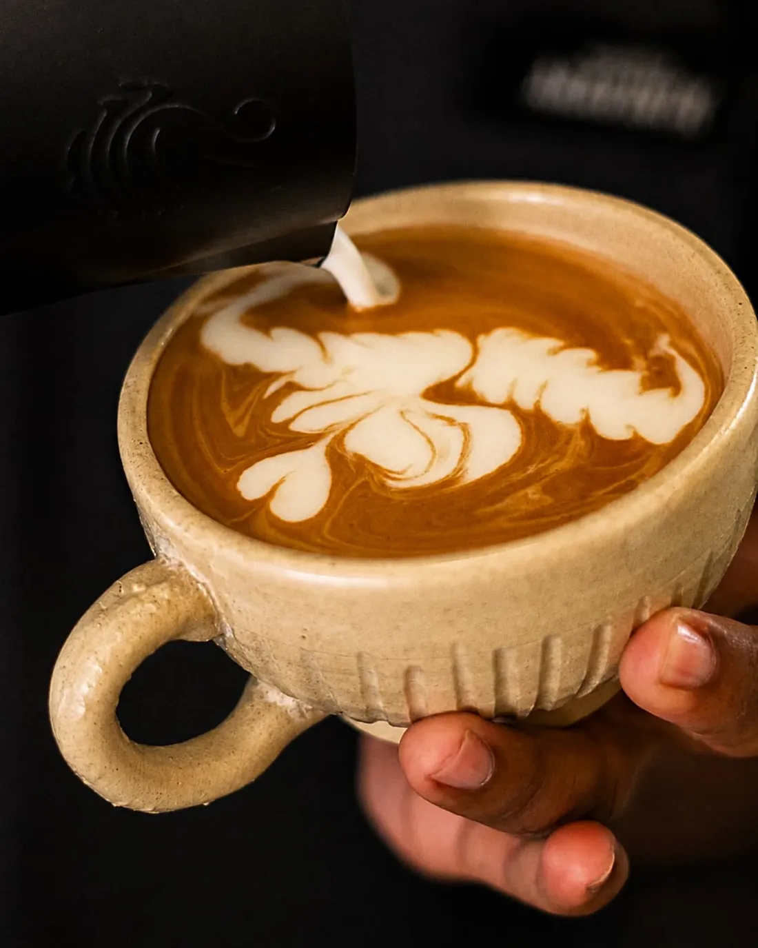 Milk poured into a fluted cream stoneware cup of espresso.