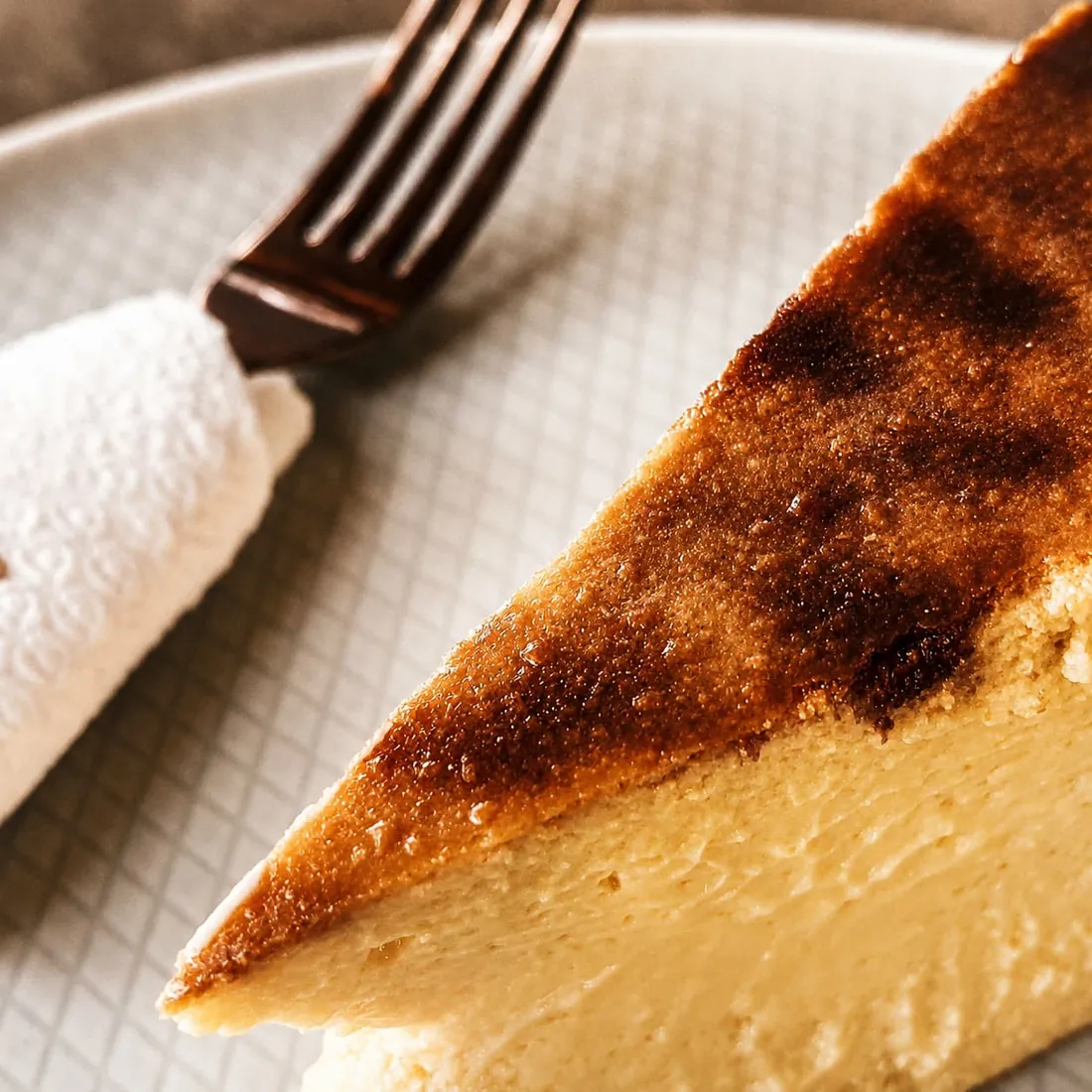 A wedge of burnt Basque cheesecake on a pale plate.